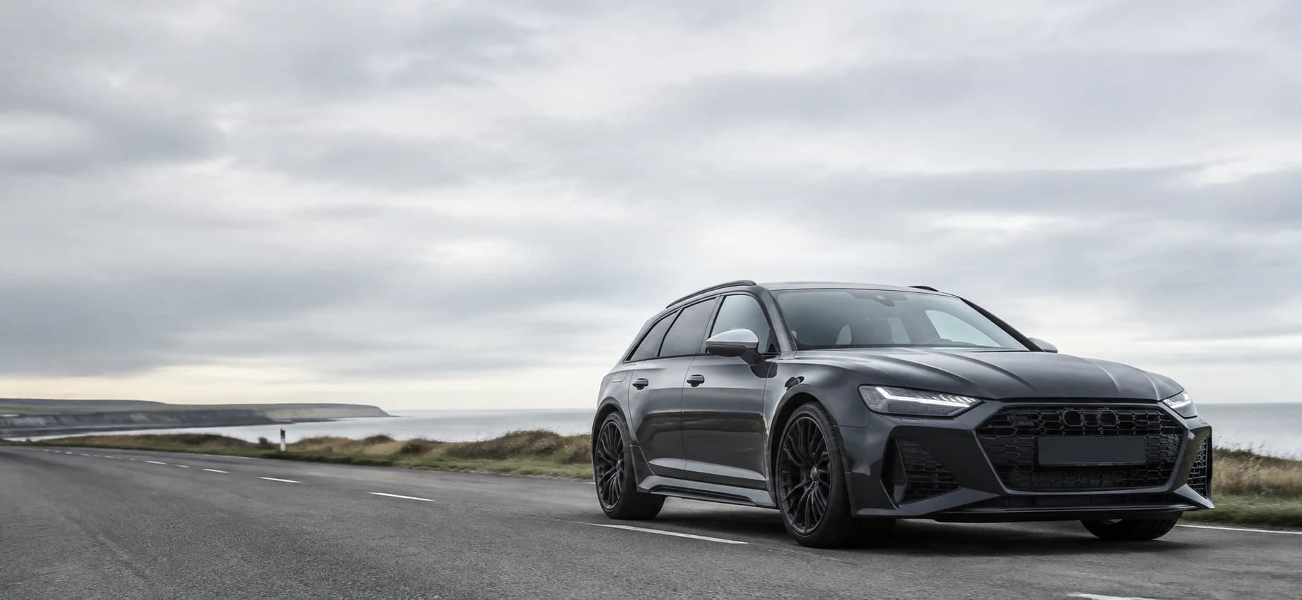 A modern dark estate car on a quiet British coastal road